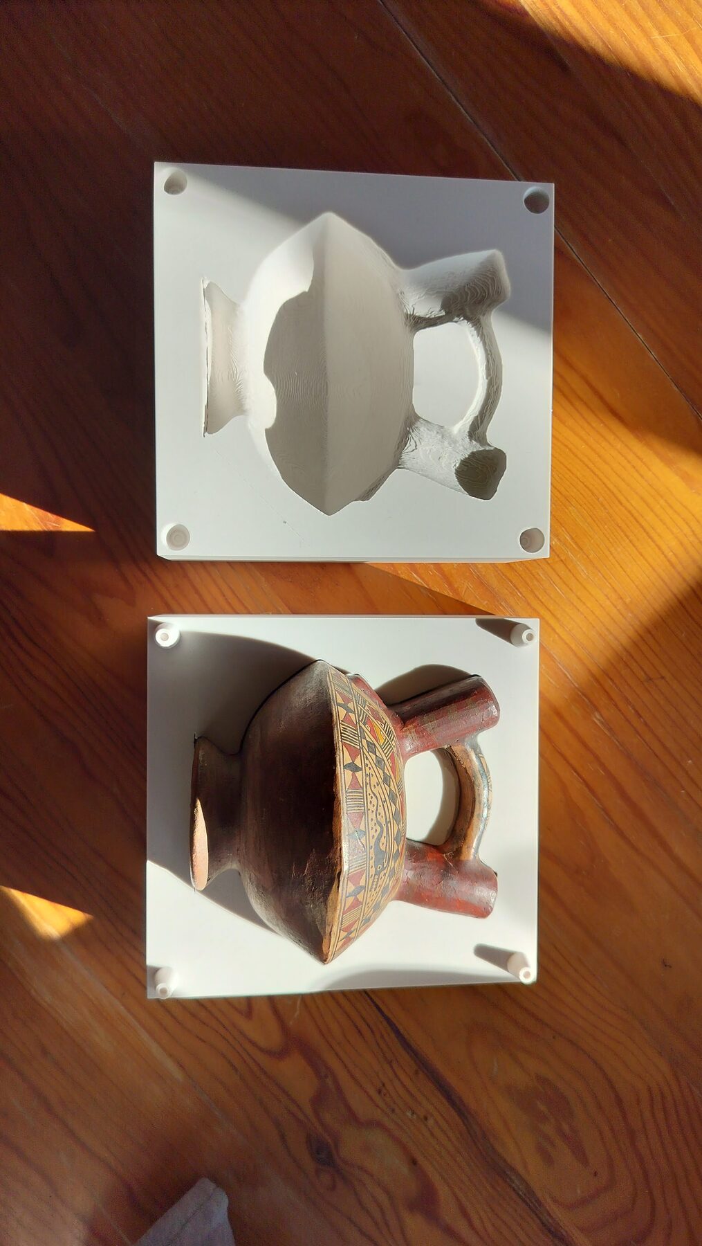 Top-down view: an empty case half above, showing the cavity and four corner sockets, and below it the vessel lying in the other half with its pins showing
